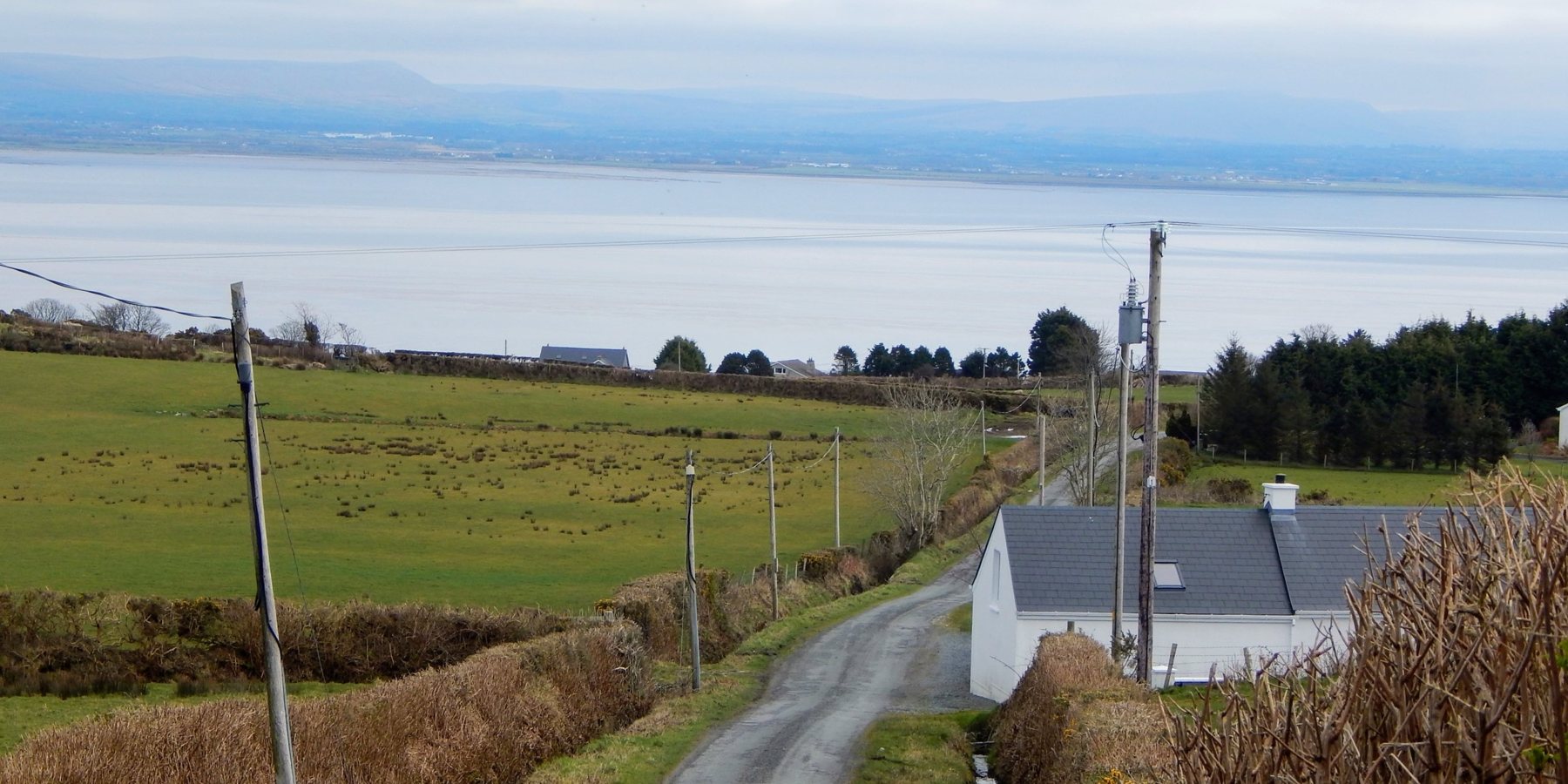 A lane running down through fields past the white McCorkell cottage at Ballyrattan to Lough Foyle, with hills on the far shore